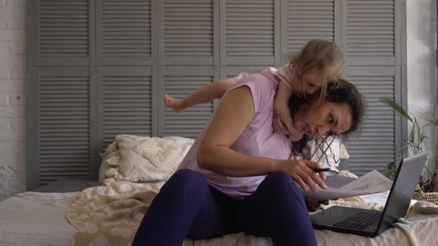 Mother freelance worker with child at workplace. Stressed business woman working from home on laptop looking worried, tired and overwhelmed. Exhausted female working remotely during economic crisis