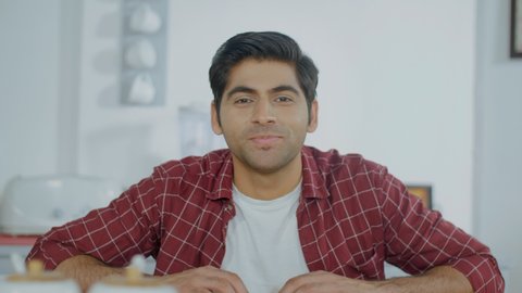 Attractive friendly-looking male looking at the webcam to greet friends or relatives. Medium shot of a young Indian man wearing casual clothes in a video conference - work from home