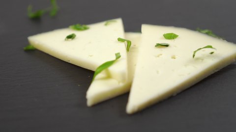 Close-up of chopped fresh parsley falls on pieces of sheep cheese. On a black stone surface. Slow motion. Dolly Shot