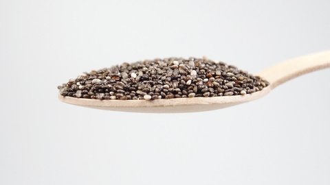 A full wooden spoon of chia seeds. Closeup chia seeds falling from a spoon. Macro shot. Slow motion