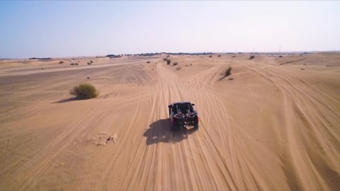 Black 4x4 truck races down an off-road path near sand dunes in the desert outside of Dubai, UAE; drone follows.