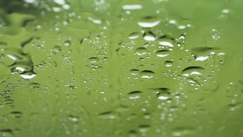Raindrops on glass window with green background. Shallow depth of field macro shot.