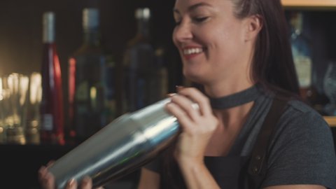 Smiling mixologist shaking craft cocktail in speakeasy bar, tilt down.