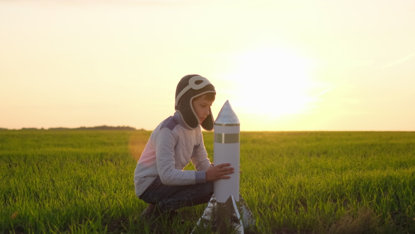 Happy little boy child in helmet aviator cosmonaut playing with toy rocket in sunset field summer nature. Kid big dream flying, astronaut, space, Concept of success leader winner, travel freedom, 4 K