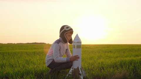 Happy little boy child in helmet aviator cosmonaut playing with toy rocket in sunset field summer nature. Kid big dream flying, astronaut, space, Concept of success leader winner, travel freedom, 4 K