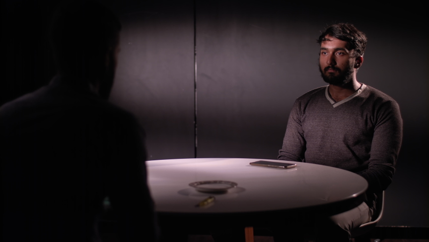 Guy sitting looking serious in a intense conversation , interrogation scene as the guy in front lights a cigarette. Shot on Ursa Mini Pro 4.6K