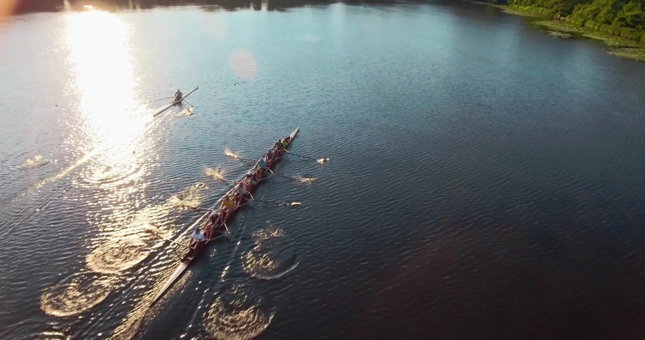 Drone shot on a sports canoe driven by a team of men and women sailing along a calm river with the sun reflected in the water. | Shutterstock HD Video #1063630525