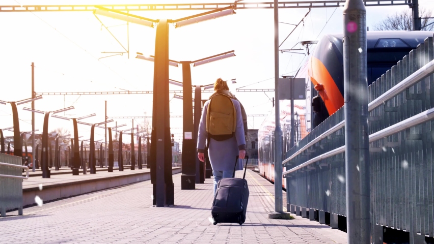 tourism, transportation and people concept - young woman with travel bag and backpack walking along empty railway station in winter