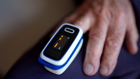 Close-up of digital pulse oximeter on senior person's finger, medical monitoring device blinking and showing oxygen saturation level on display. Senior adult controlling oxygen rate in blood during