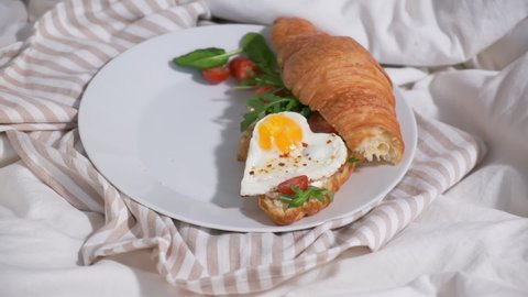 Valentine's day concept. Woman eating breakfast in bed on Valentine's Day. Sandwiches with croissant, bagel, cream cheese and fried eggs hearts on white bed.