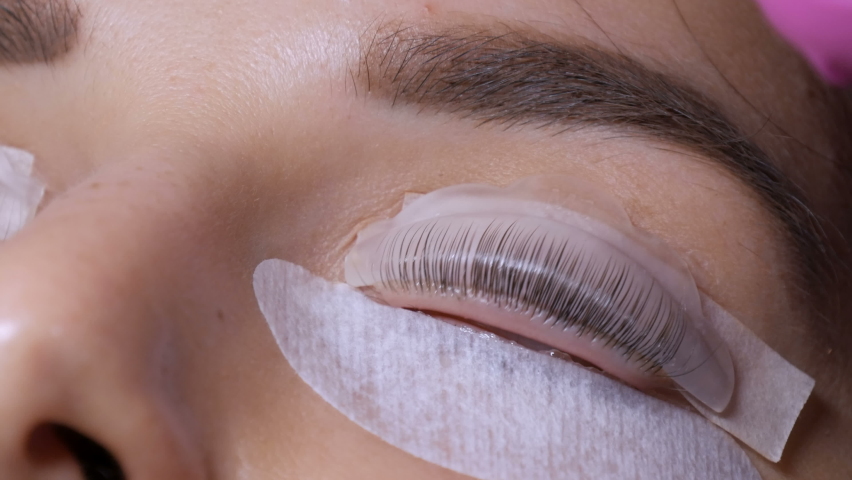 Face of a young girl before a modern eyelash lamination procedure in a professional beauty salon. The master applies special glue before the eyelash curling procedure in pink rubber gloves close up. Royalty-Free Stock Footage #1063642102