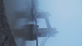 Vertical video of Tower Bridge and River Thames in foggy and misty weather conditions in London City Centre on blue atmospheric morning with mist and fog in Coronavirus Covid-19 lockdown, England, UK