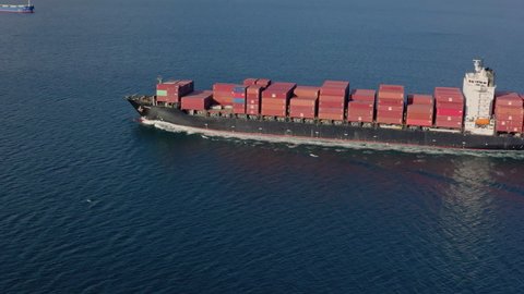 Aerial view large ship with red containers sails on calm sea on a sunny morning. Concept of delivery of goods from abroad, maritime trade, logistics. Drone high quality footage