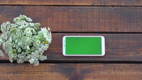 Closeup top view flatlay 4k video of modern smartphone laying on brown wooden surface. Screen of device with empty blank green color. - Powered by Shutterstock - Get 15% off with code: PIKWIZARD15