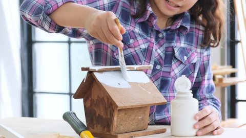 Young girl painted white wooden toy house she made herself on carpenter's table at home,slow motion.