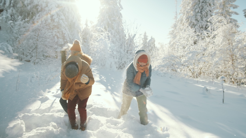 Group of young excited male and female friends playing snowballs and throwing snow in forest while having fun outdoors on sunny winter day | Shutterstock HD Video #1063651522