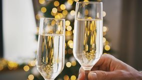Hands of unknown people who cheering with glasses of champagne against Christmas tree decorated with glowing garland. Blurred background, bokeh. Happy New Year. Close up, slow motion - Powered by Shutterstock - Get 15% off with code: PIKWIZARD15