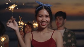 Beautiful Young woman and group teenage asian playing sparklers dance celebrating new years eve at sunset on beach with ocean background