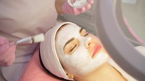 Skin care procedure. professional beautician applies a white mask to the client's face chin and cheek. Video footage. Relaxed woman having spa salon time for herself. Beauty blogger