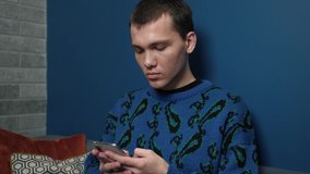 Young handsome caucasian Man Uses Smartphone at Home. Man Browses Through Internet, Watches Videos and Uses Social Networks at Home.