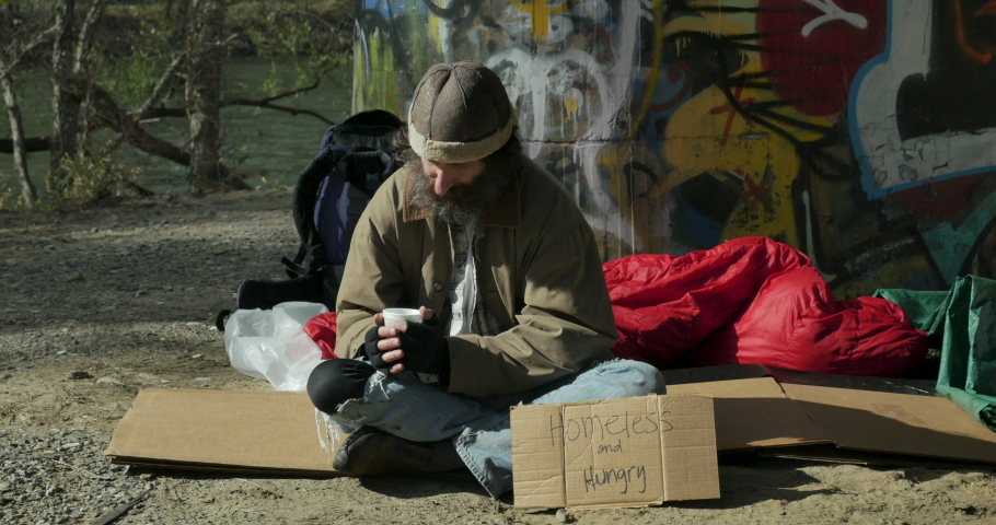 Woman giving a take away container of food to a hungry homeless man sitting outside with a homeless and hungry cardboard sign Royalty-Free Stock Footage #1063658989