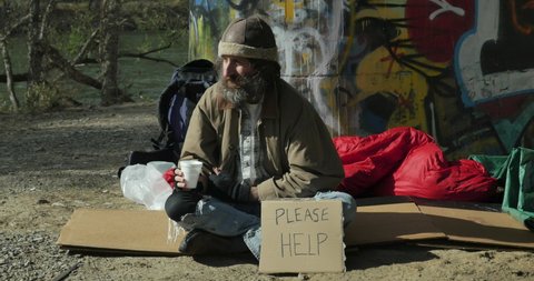 Woman giving money to a homeless man begging on the street with a please help cardboard sign - wide shot