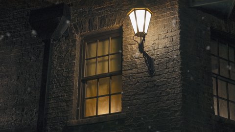 Dark Christmas or winter night in London alley way with gas street lamp and snow falling.