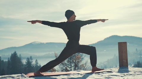 Caucasian senior man doing yoga exercises in front of amazing sunset on the winter mountains