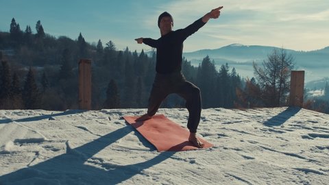 Caucasian senior man doing yoga exercises in front of amazing sunset on the winter mountains