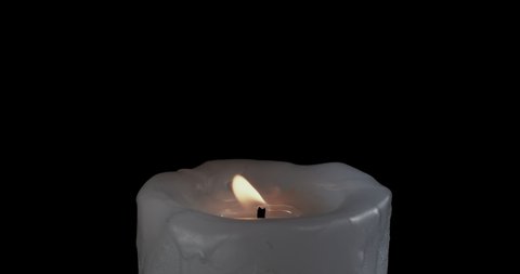 A single white candle burning.Isolated candle burning with dark background.White paraffin candle with yellow shades burns on a black background.Background or illustration of remembrance or celebration