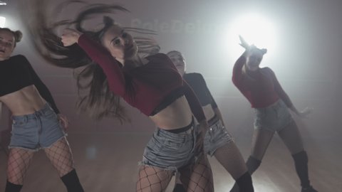 Young sexy womans in shorts dancing dancehall in dark smoky dance studio. Group of young dancehall dancers