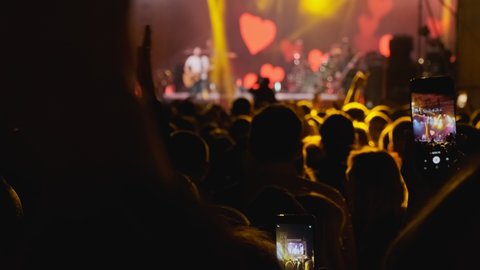 Big crowd at concert cheering clapping hands at night rock concert. Silhouette hands of audience crowd people use smart phones enjoying the concert. 4k, UHD