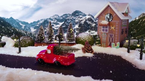 Christmas winter scenery with pickup truck driving with Christmas tree on car trunk. It is snowing in Christmas village. Stop motion with model of festive Christmas city and mountains landscape