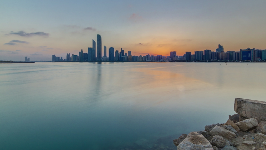 Abu Dhabi city skyline on sunrise time with water reflection timelapse from the breakwater near cultural village. Few clouds on morning sky | Shutterstock HD Video #1063666507