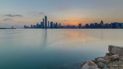 Abu Dhabi city skyline on sunrise time with water reflection timelapse from the breakwater near cultural village. Few clouds on morning sky