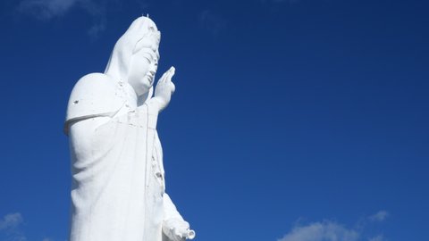 Huge Japanese Buddha against the backdrop of the blue sky and moving white clouds. Goddess of Mercy