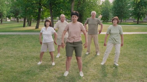Wide shot of group of five old people having Qigong training on lawn in park