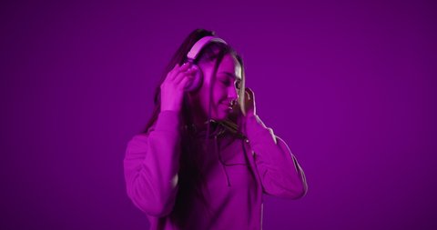 Carefree young brunette woman hipster with ponytail, dressed in hoodie, listening music in headphones, dancing rhythmically to audio beat.