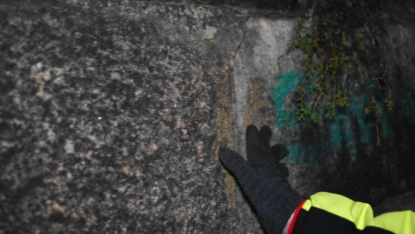 A guy walks along the embankment at night and touches the stones with his hand. Shooting on the move.