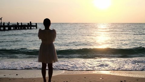Asian broken heart girl standing at beach looking at sunset or sunrise with lonely feeling. Asian broken hearted woman come to the sea alone for vacation. Asian woman loves sunset or sunrise concept.