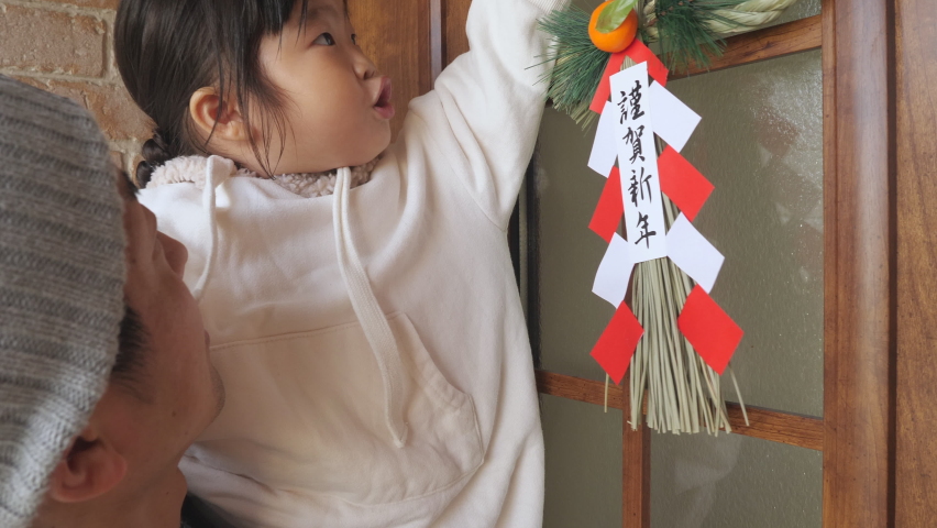 Asian girl who attaches a New Year decoration to the front door of the house. Chinese character Kinga Shinnen is written as Happy New Year. Traditional Japanese event. Displayed before New Year