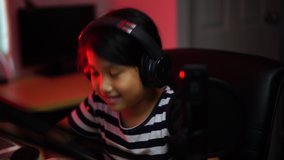 Young Asian girl e-sport gamers wearing headphone and concentrated while live streaming vlog online video game battle from home. e-sport video game competition, new normal, gamer and vlog concept