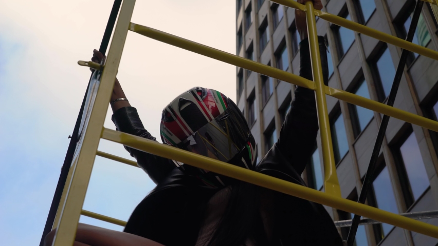 A woman in a sexy bodysuit and a helmet is dancing on the street in a yellow cage.