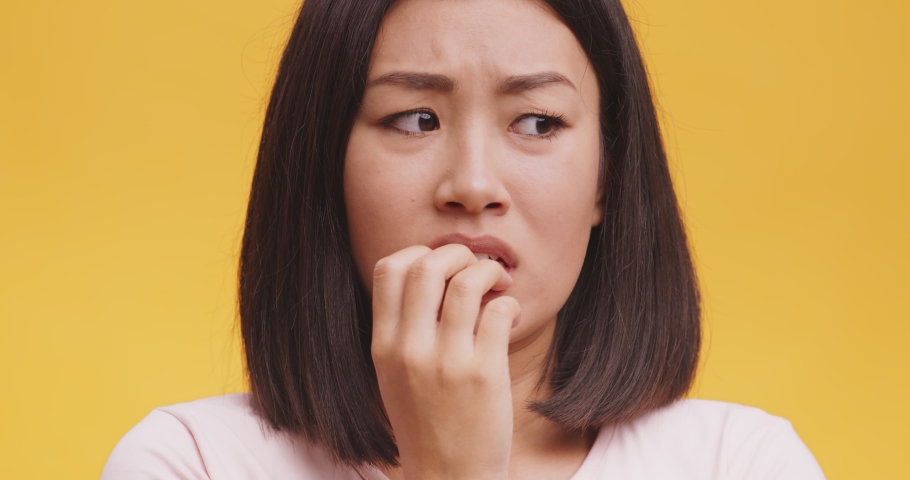 Nervous asian woman feeling panic, biting her nails, feeling worried and confused, orange studio background, close up portrait Royalty-Free Stock Footage #1063677322