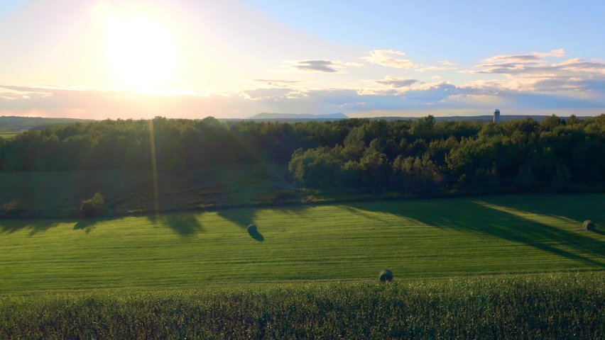 Aerial shot moving laterally over a field of wheat bales under a beautiful sunset