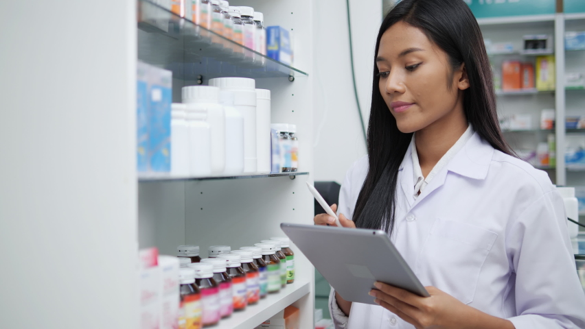 Asian pharmacists working and checking drug in pharmacy store at hospital. Asian doctor checking medicine cabinet and wearing white medical coat. Shelves pharmacy background in drugstore. | Shutterstock HD Video #1063681210