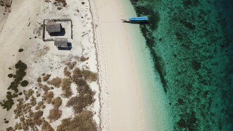 A drone shot of a boat anchored to a beach on an island near Maumere, Indonesia. Clear, turquoise coloured water displaying coral reef. Deeper and darker see in the back. Fishing boat. Serenity
