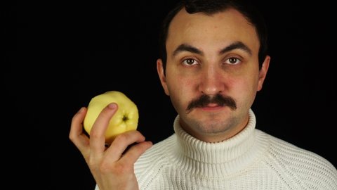Man with mustache eating healthful green apple over black background.