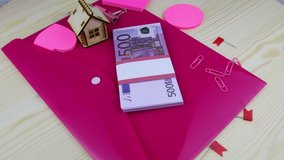 A pack of 500 euros of bills is lying with pink stationery rotating on the table