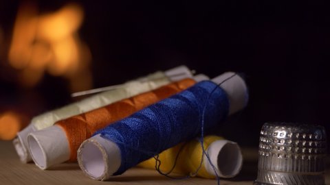Coils of colored thread and a thimble rotate against the background of the fireplace flame. Close-up shooting.
